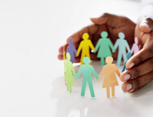 A photograph of multi-colored people made of paper holding hands in a circle, with a person's hands holding the figures